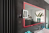A wall mirror with integrated red LED lighting on a grey-tiled wall