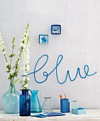 Various blue vases against a wall with the word 'blue' knitted on the wall