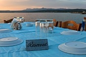 Gedeckter Tisch mit pastellblauer Tischdecke vor griechischer Küstenlandschaft