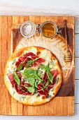 A pizza with gorgonzola, ham, rocket and honey