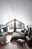 Pleasant attic room with white, wood-clad walls, rocking sheep. comfortable bed and glass gable-end wall