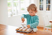 A young boy dusting muffins with icing sugar