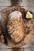 A whole loaf of wholemeal bread on a baking stone with a butter dish