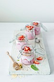 Jars of strawberry yoghurt with honey and mint on a white chopping board