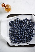 Fresh blueberries on a baking tray lined with baking paper being drizzled with honey