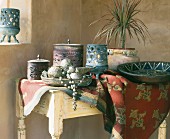 Schalen und Behälter mit Deckel auf Tischtuch und Tisch in Zimmerecke, in orientalischem Stil