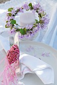 Candle lantern decorated with wreath of purple flowers and bird ornament made from glittering pink beads on place setting