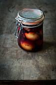 Pickled eggs with onion skins and a spiced liquid in a jar on a wooden table