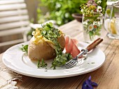 Baked potato with herb sauce outside on a garden table