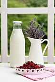 A bottle of milk, a jug of lavender and fresh berries on a garden table