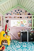 Little girl seen through window of wooden play house painted in pastel colours decorated with toy figurines