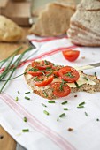 A slice of potato bread topped with butter, tomatoes and chives