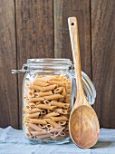 A jar of wholemeal penne with a wooden spoon