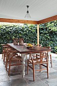 Classic chairs around rustic dining table on roofed terrace