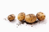 Four dirty potatoes on a white surface