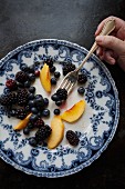Peaches, blackberries and blueberries on a blue-and-white patterned plate with a fork