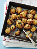 Hasselback potatoes with herbs on a baking tray (seen from above)