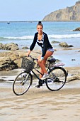 A blonde woman cycling along a beach