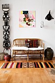 Patterned rug on wooden floor in front of cane couch with cushions next to ethnic sculpture hung on wall