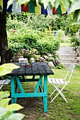Rustic garden table with turquoise-painted frame and folding chairs in front of steps in garden