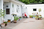 Pflanzentöpfe auf gepflasterter Terrasse, vor Haus mit teilweise holzverschalter Fassade in Weiß