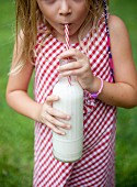 A little girl drinking a bottle of vegan milk in a garden