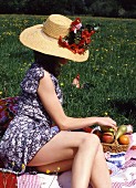 Frau in kurzem Sommerkleid und Strohhut bei Picknick