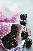 blackberries in a a pink paper bag and on a dessert spoon