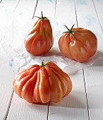 Three beefsteak tomatoes on a white wooden surface
