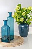 Two blue glass bottles on wooden tray and ceramic vase of lime-green hydrangeas