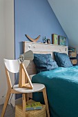 Double bed with rustic wooden headboard against blue wall, blue satin bed linen and table lamp on designer wooden chair