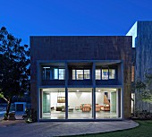 View from garden to contemporary house with illuminated interior at twilight