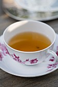 Kräutertee in weißer Teetasse mit traditionellem weinrotem Blumenmuster
