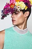 Junger Mann in türkifarbenem, ärmellosem Pulli mit Blumenschmuck auf dem Kopf