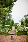 Steinbecken auf gekiestem Weg in angelegtem Garten mit Hecken und Rosen