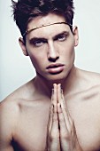 A young man wearing a crown of thorns holding his hands together in prayer