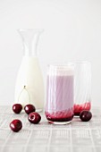 A cherry milkshake with a jar of milk and fresh cherries