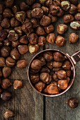 Hazelnuts in a copper cup and on a wooden surface