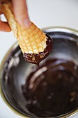 An ice cream cone being dipped into melted chocolate