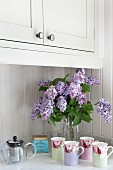 Vintage-style beakers and vase of lilac on kitchen counter with Carrara marble worksurface
