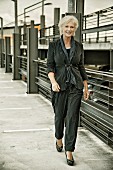 A blonde woman wearing black cord trousers and a jacket in a multi-storey car park