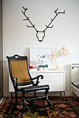 Antique Scandinavian rocking chair in front of metal cabinet below stylised stag's head made from black washi tape on white wall