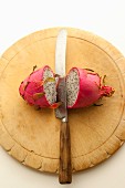 A halved dragon fruit on a wooden board with a knife