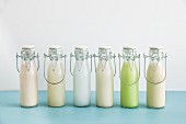 Various types of milk substitutes in bottles with their ingredients: almond milk, rice milk, coconut milk, oat milk, Edamame milk and soya milk