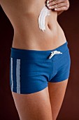 A woman wearing tight, blue, sporty shorts applying moisturiser to her stomach