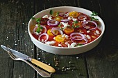 A colourful tomato salad with red onions and feta cheese on an old wooden table