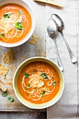 Two bowls of tomato soup garnished with Parmesan crisps, sour cream and fresh basil