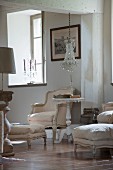 Rococo armchair with pale cover and side table with turned and carved pedestal base below chandelier with glass pendants