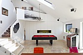 Pool table in open-plan games area and staircase leading to gallery in contemporary building