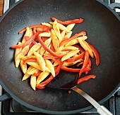 Potato orzo pasta and pepper strips being fried in a wok
